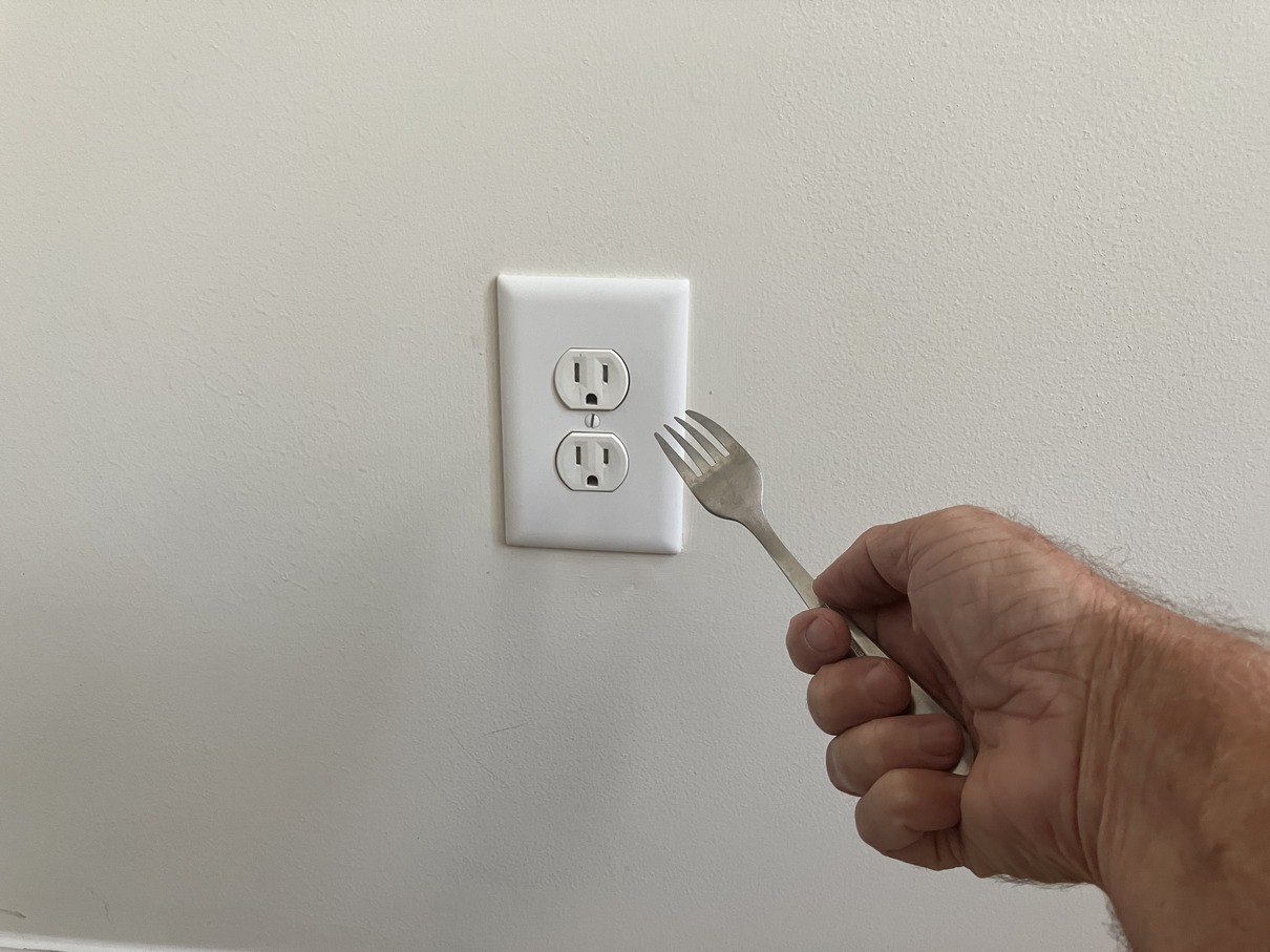 hand holding fork near electrical outlet